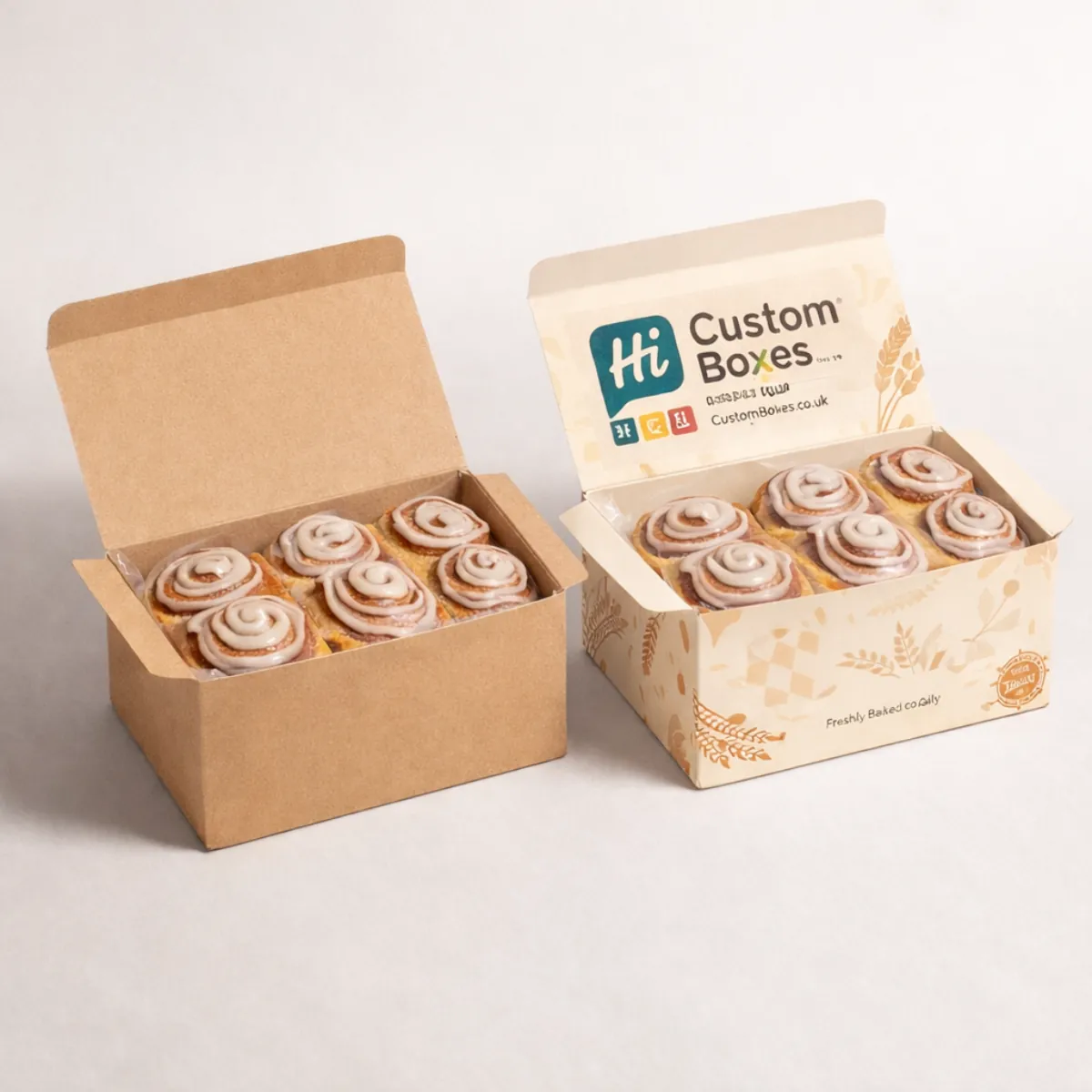 Two rectangular bakery boxes containing six glazed cinnamon buns, featuring a plain brown and a printed design. class=